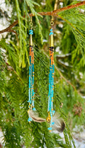 Extra long turquoise and gold beaded earrings with feathers on a cedar branch.