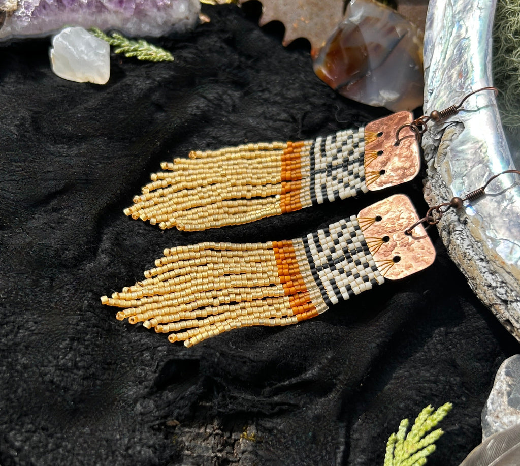 Pair of beaded earrings on a dark fabric background with crystals and nature elements.