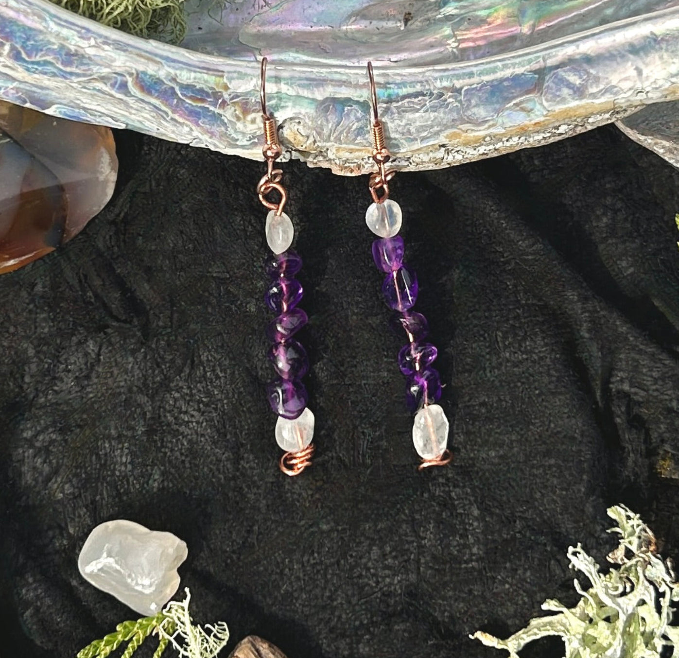 Pair of dangle earrings with purple amethyst and blue moonstone beads on a black background.