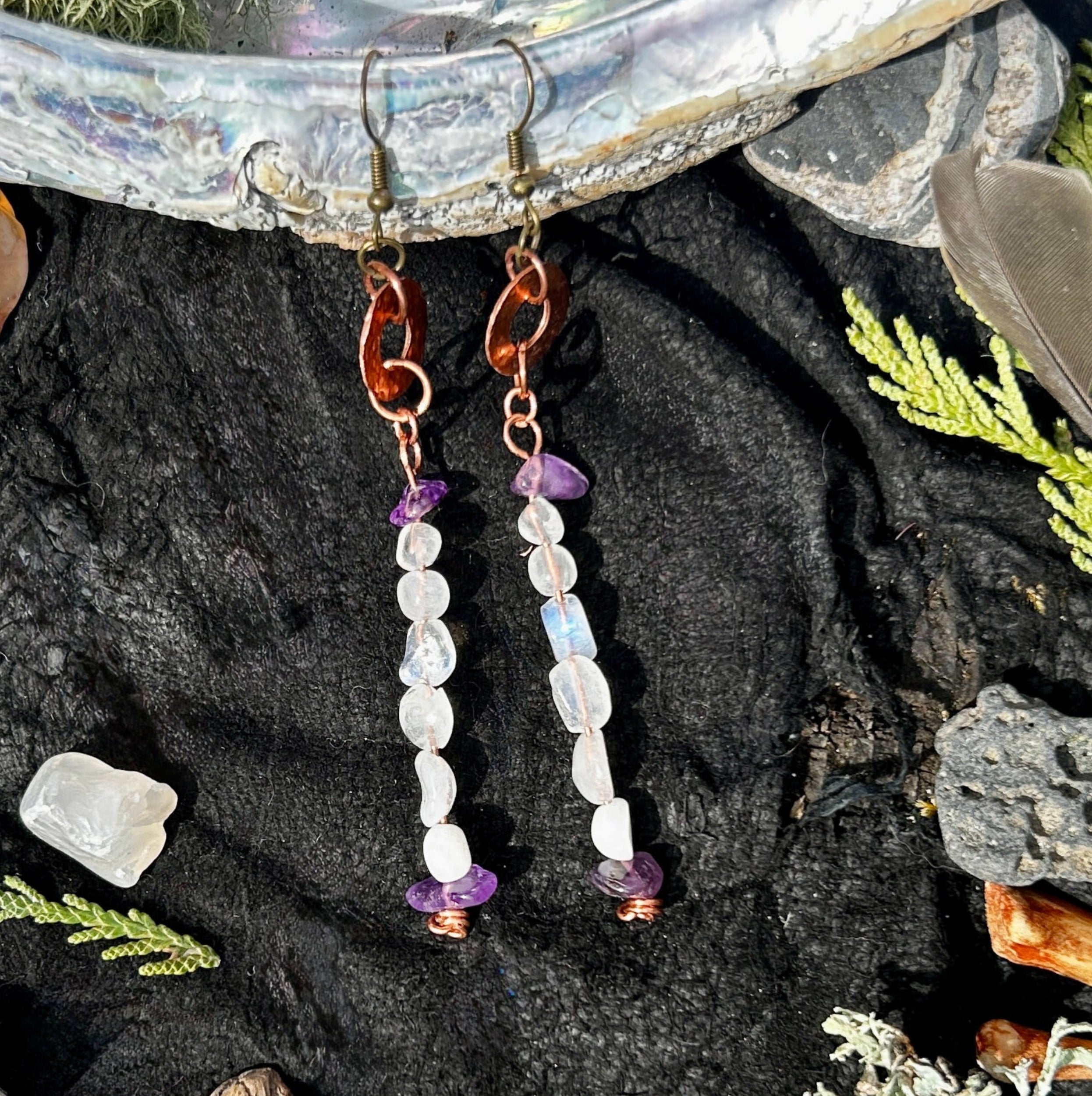 Pair of copper earring with white and blue moonstone beads and purple amethyst beads on a black background. 