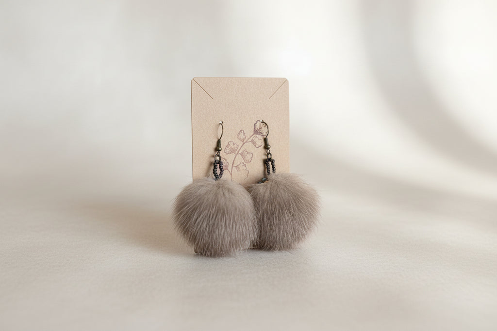 Round brown fur earrings with sparkling blue and chocolate brown beaded edging hanging on a brown display card. 