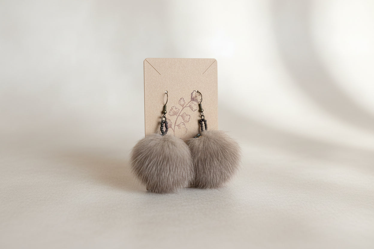 Round brown fur earrings with sparkling blue and chocolate brown beaded edging hanging on a brown display card. 